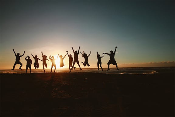 Silhouettes of people jumping on beach at sunset